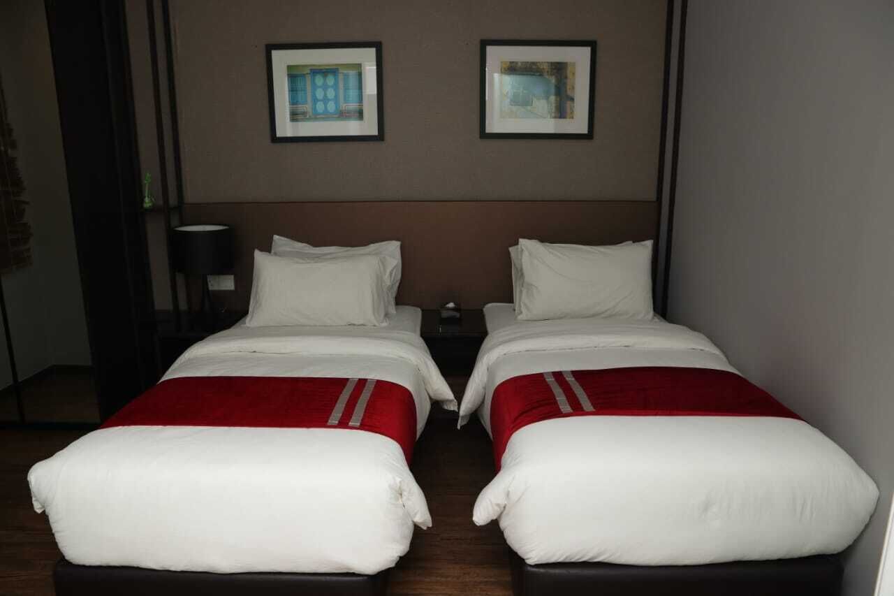 A hotel room with two single beds, a nightstand, a lamp, and two framed pictures on the wall.