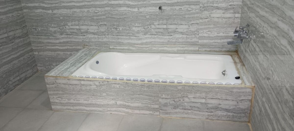 Una bañera rectangular con un revestimiento de pared que imita el mármol.