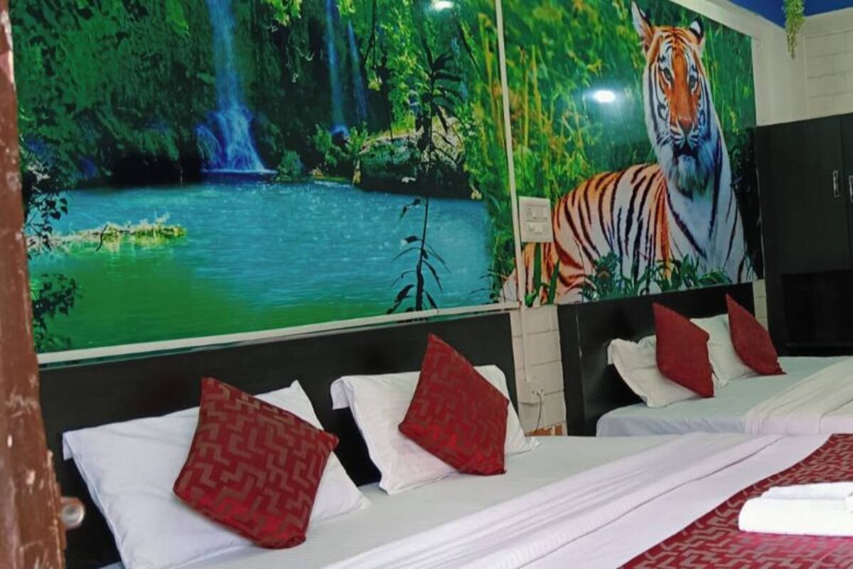 Une chambre d’hôtel avec deux lits, une literie rouge et blanche, une grande fresque représentant un tigre sur le mur, et une vue sur une cascade.