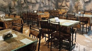 Ein Restaurant mit Tischen, Stühlen, einer Felswand-Mural und einer Deckenleuchte.