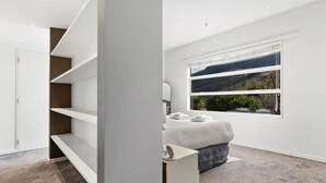 Een moderne slaapkamer met een bed, een groot raam met uitzicht, inbouwplanken en een garderobe.