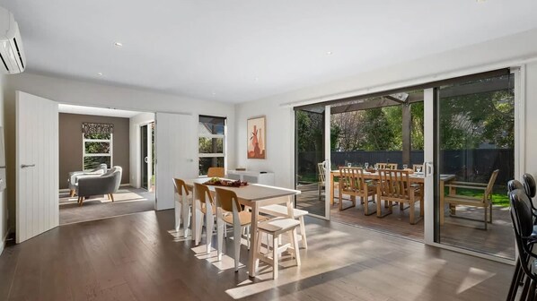 A spacious dining area with a large table and chairs, a separate seating area with a sofa, and a sliding glass door leading to an outdoor patio.