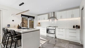 Een moderne keuken met witte kasten, een ingebouwde oven en een groot kookeiland met barstoelen.