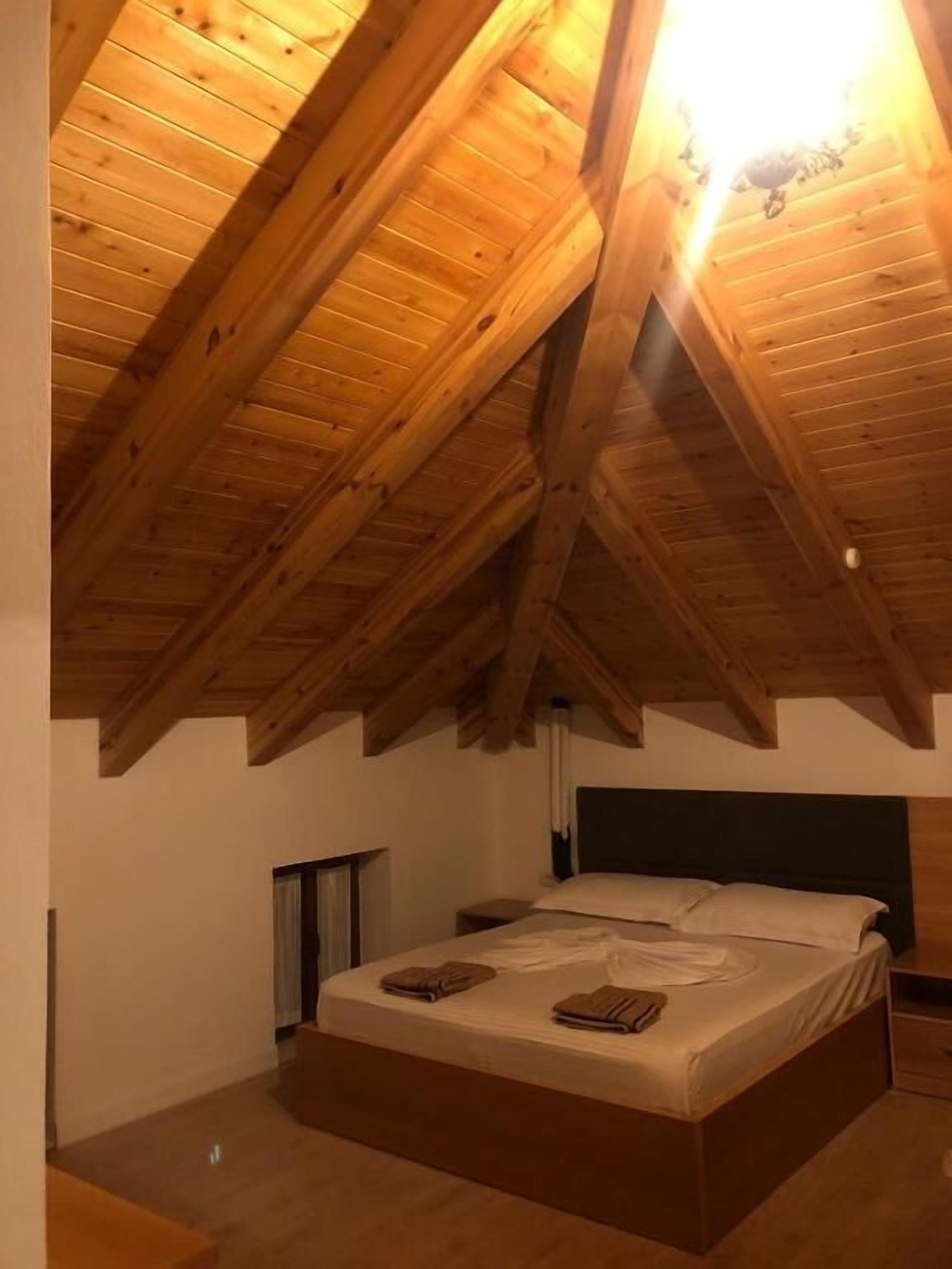 Une chambre avec un plafond en bois incliné, un lit avec des oreillers et une table de chevet.