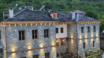 A stone building with multiple windows and a paved outdoor area with chairs and tables.