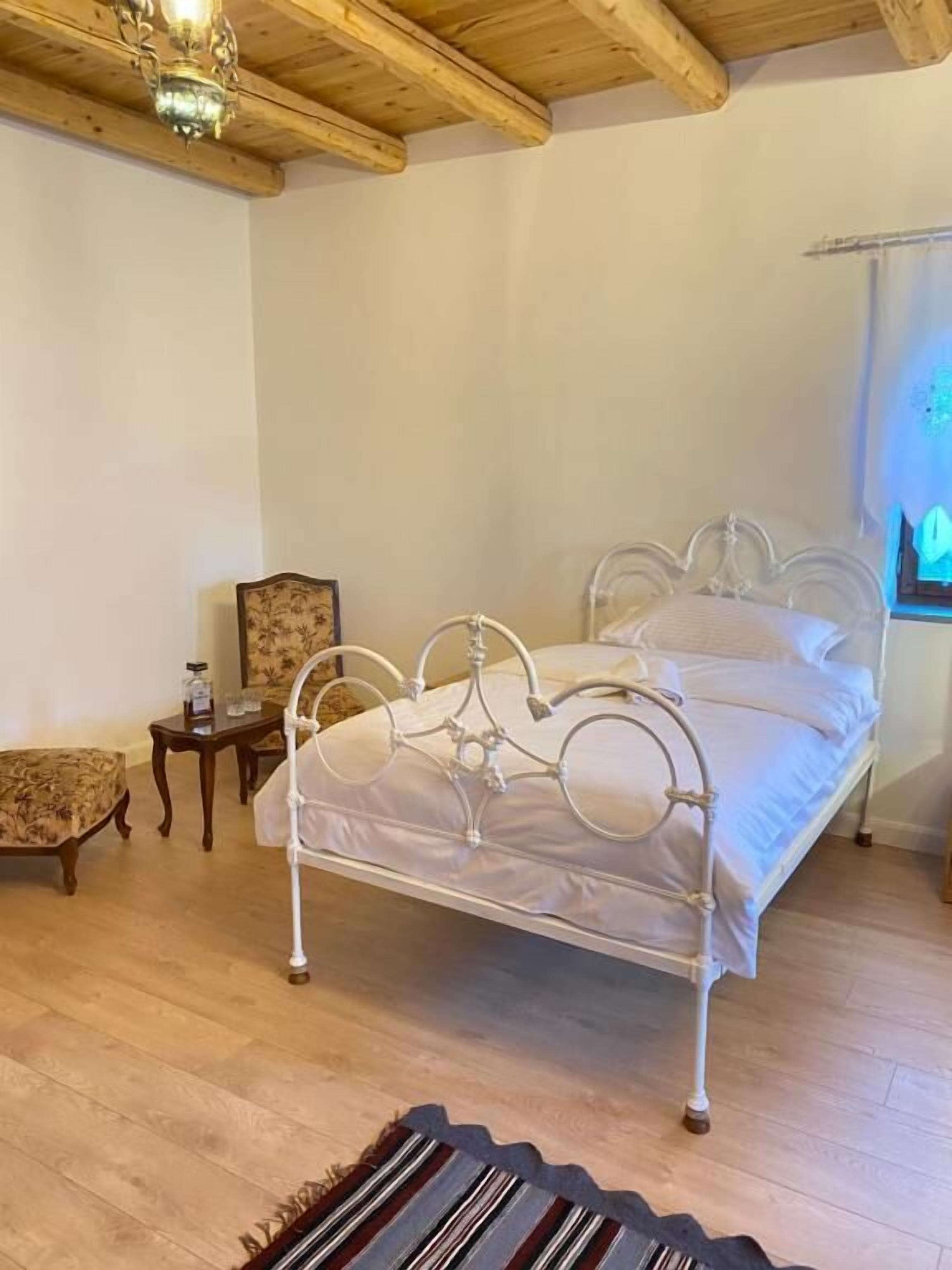A bedroom with a metal bed frame, a wooden floor, a small wooden table, and a chair.