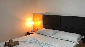 Uma cama bem arrumada com lençóis brancos, duas toalhas enroladas e uma luminária de cabeceira.