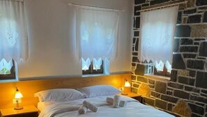 Een slaapkamer met een houten hoofdeinde, een groot bed met witte lakens, twee bedlampen en een stenen muur.