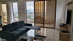 A modern living room with a sofa, a glass coffee table, and a TV on a wooden stand.