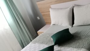 A modern hotel room with a wooden headboard, a bed with white and green bedding, and a view of the outside through a window with curtains.