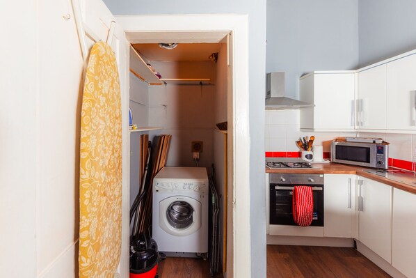 Compact kitchen with a washing machine, microwave, and white cabinets with silver handles.
