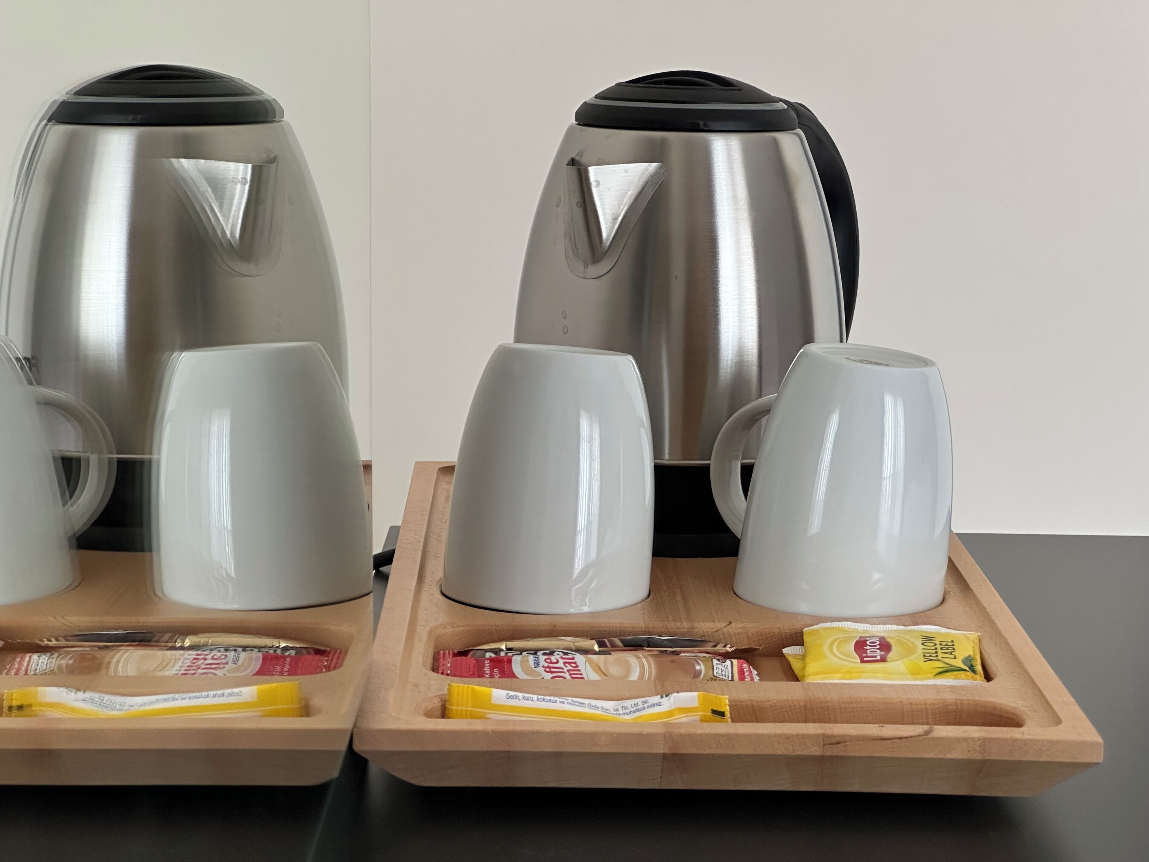 Two stainless steel kettles on a tray with white cups and packets of coffee and tea.