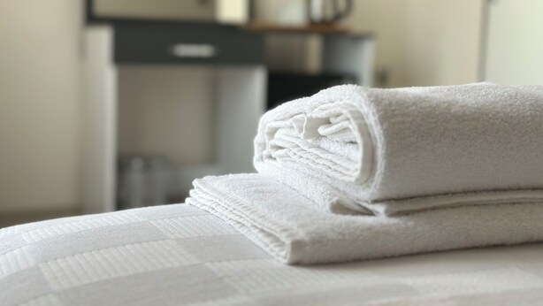 A neatly folded white towel on a bed with a textured white bedspread. - Şirin Garden Ayvalık (Ayvalik)