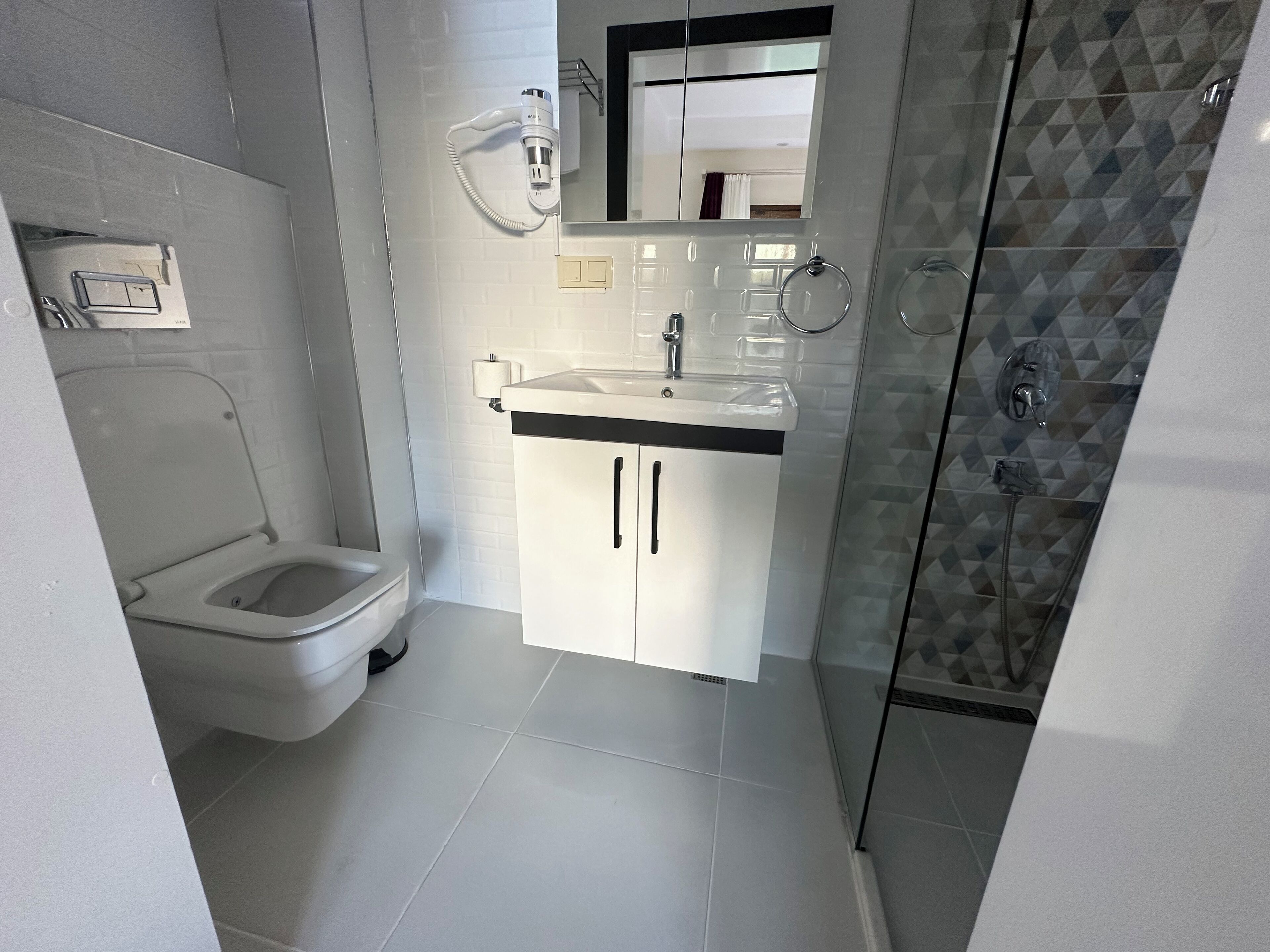 Un baño moderno con inodoro, lavabo con espejo y zona de ducha.