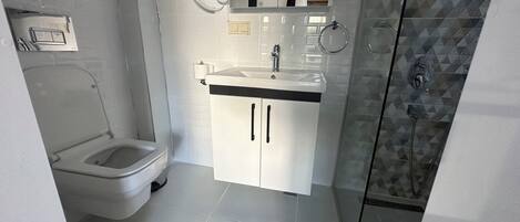 Une salle de bain moderne comprenant des toilettes, un lavabo avec un miroir au-dessus, et un espace douche.