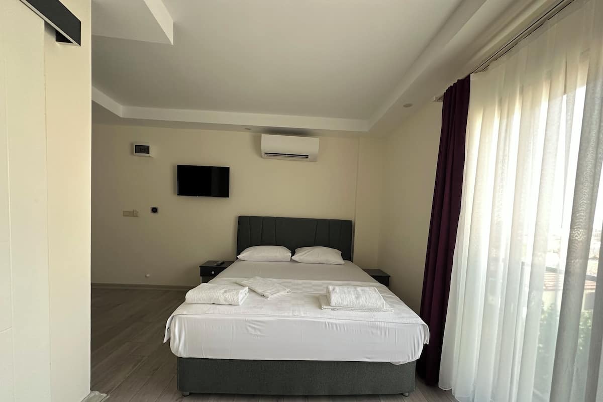 A modern hotel room with a large bed, a flat-screen TV, and an air conditioning unit on the wall.