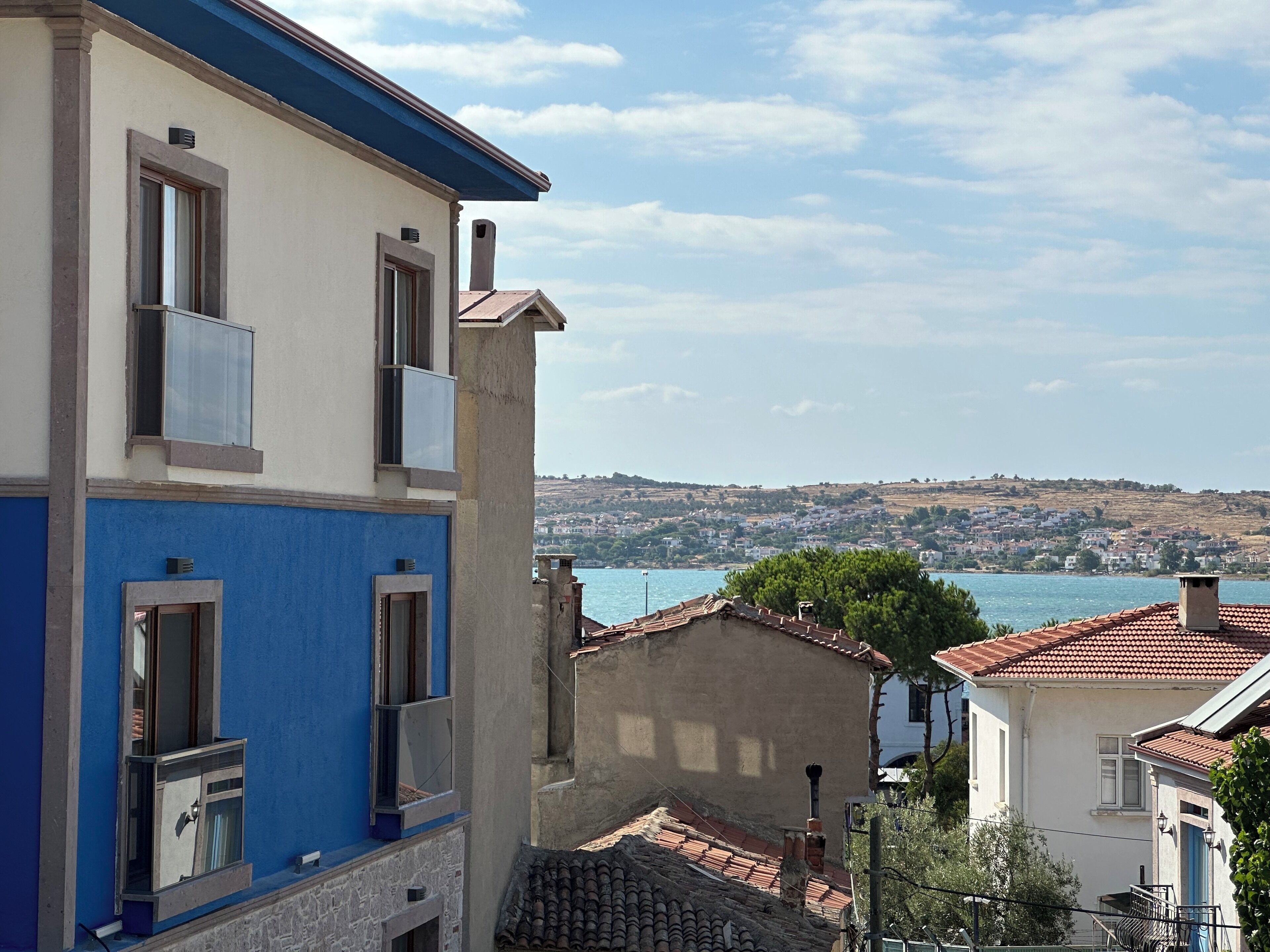 Un bâtiment situé sur la côte, doté d’une façade bleue, d’une fenêtre bien visible et offrant une vue sur la mer et les collines lointaines.