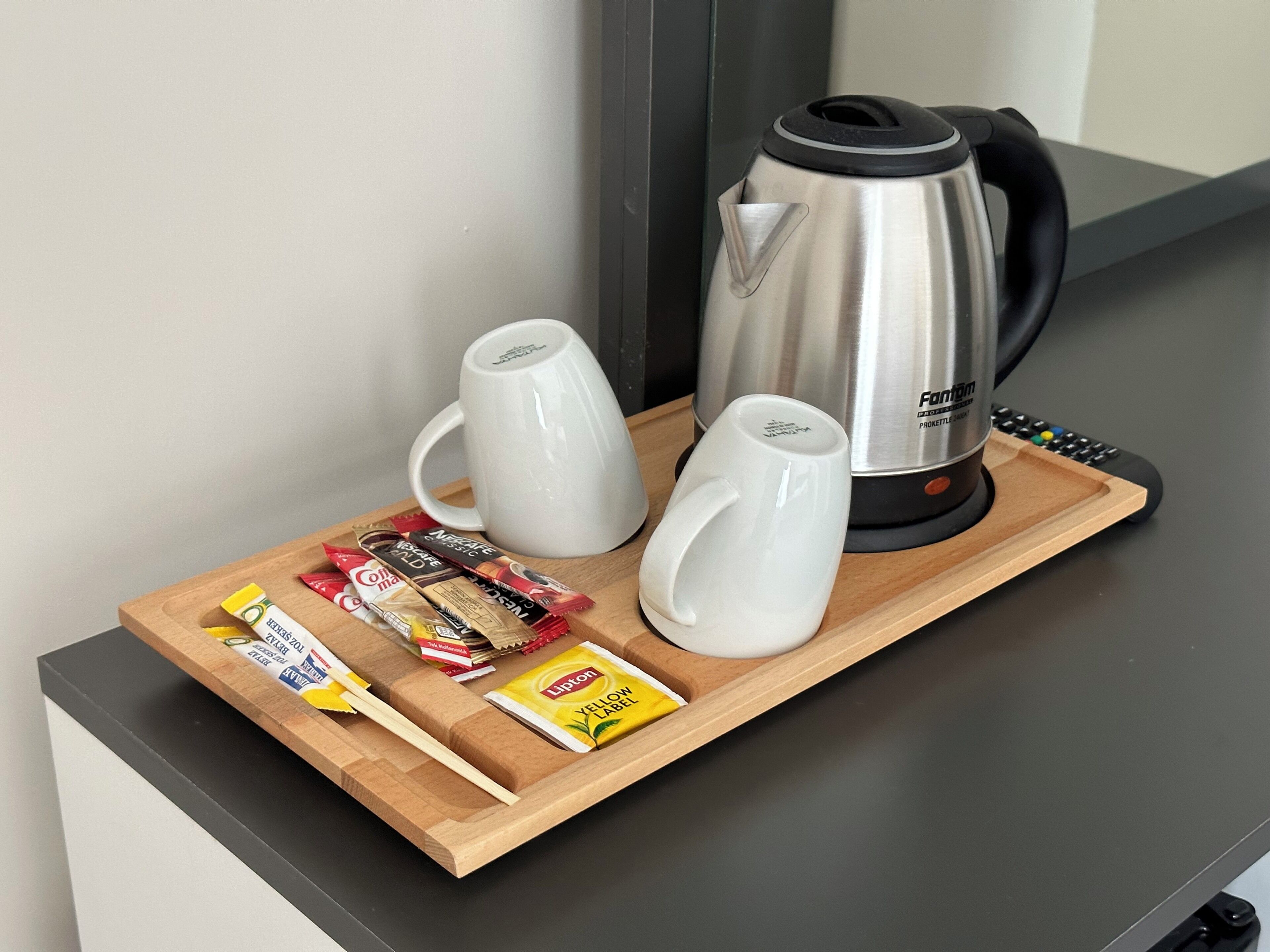 Een dienblad met een waterkoker, twee mokken en snacks, waaronder Lipton thee en chocoladerepen.