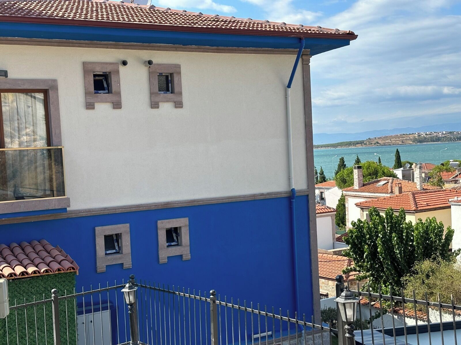 A two-story building with a blue and white facade, a tiled roof, and a view of a coastal landscape.