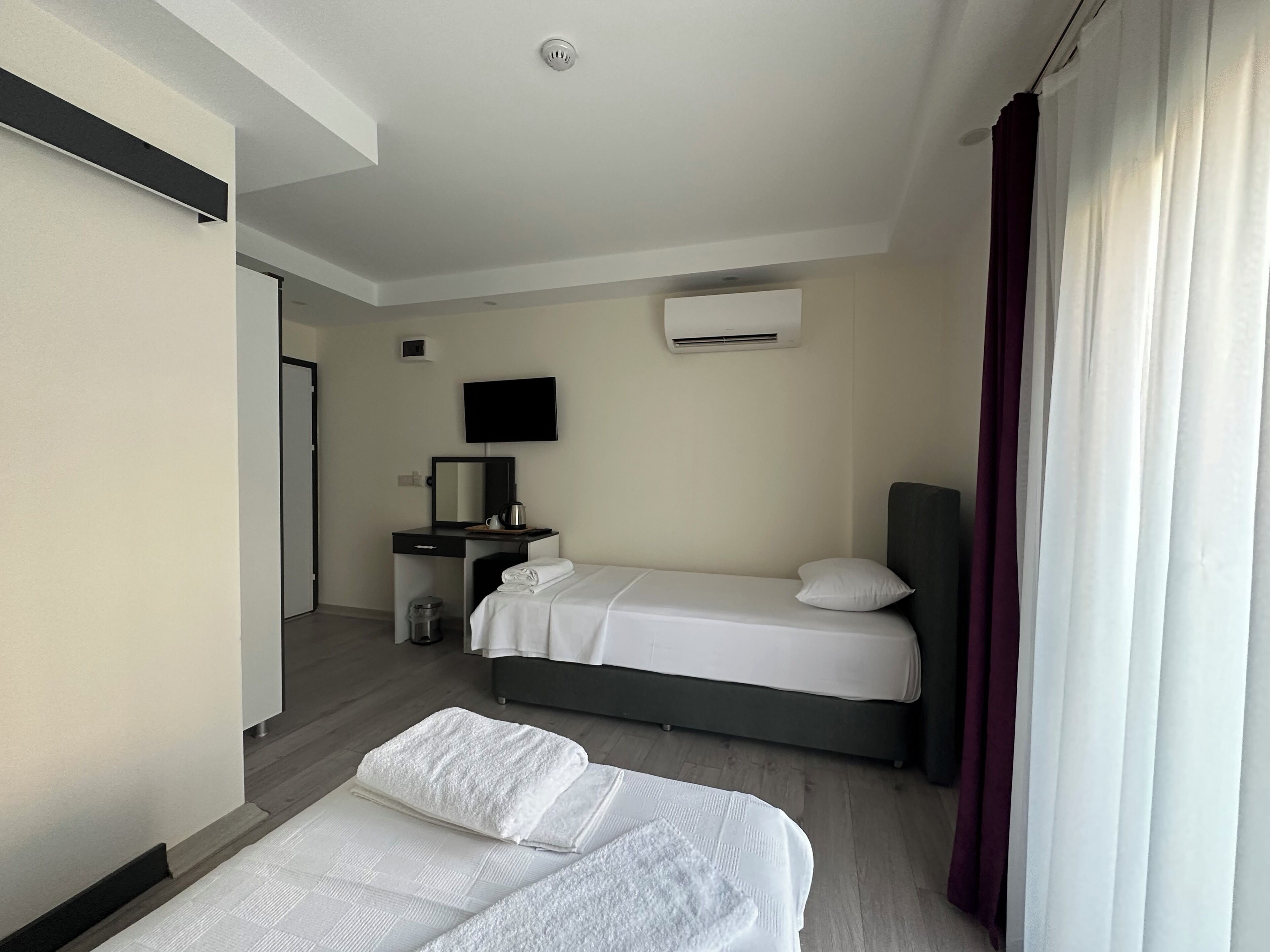 A hotel room with two beds, a desk with a mirror, a television, and an air conditioning unit.