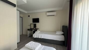A hotel room with two beds, a desk with a mirror, a television, and an air conditioning unit.