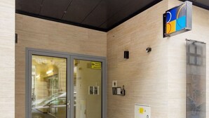 Ein Gebäudeeingang mit Glastür, kleinem Schild und Feuerlöscher an der Wand.