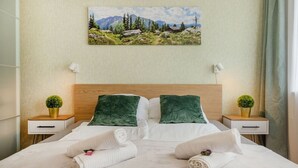 Ein ordentlich bezogenes Bett mit zwei Kissen, zwei Nachttischen mit Lampen und einem Gemälde einer Berglandschaft an der Wand.