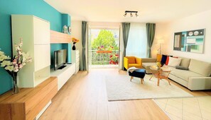 A modern living room with a TV, sofa, and a balcony with flowers. - FEEL HOME DELUXE (Budapest)