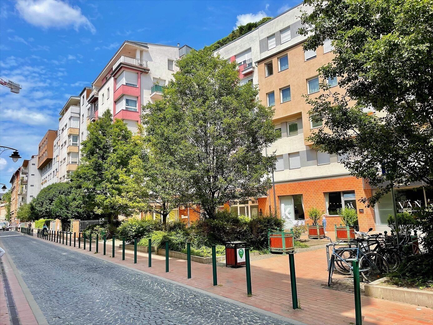 Une rangée d’immeubles d’appartements modernes dotés de balcons, une rue pavée et des vélos garés devant.