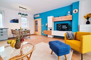 A modern living room with a blue accent wall, a yellow sofa, a dining area with a glass table, and a kitchen visible in the background. - FEEL HOME DELUXE (Budapest)