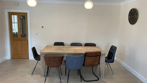 A dining area with a wooden table and six chairs, two pendant lights, a wooden door, and a wall clock. - Beautiful Home Near Lough Corrib (Carrowmoreknock)