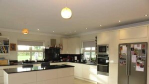 A modern kitchen with white cabinetry, a central island, a built-in oven, and a refrigerator with notes attached. - Beautiful Home Near Lough Corrib (Carrowmoreknock)