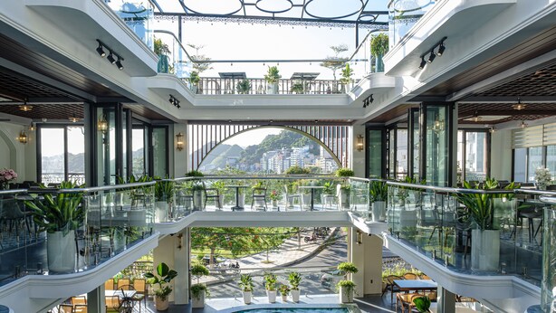 A multi-level indoor space with a central pool, glass railings, and multiple dining areas with outdoor views. - Roza Palace (Hai Phong)