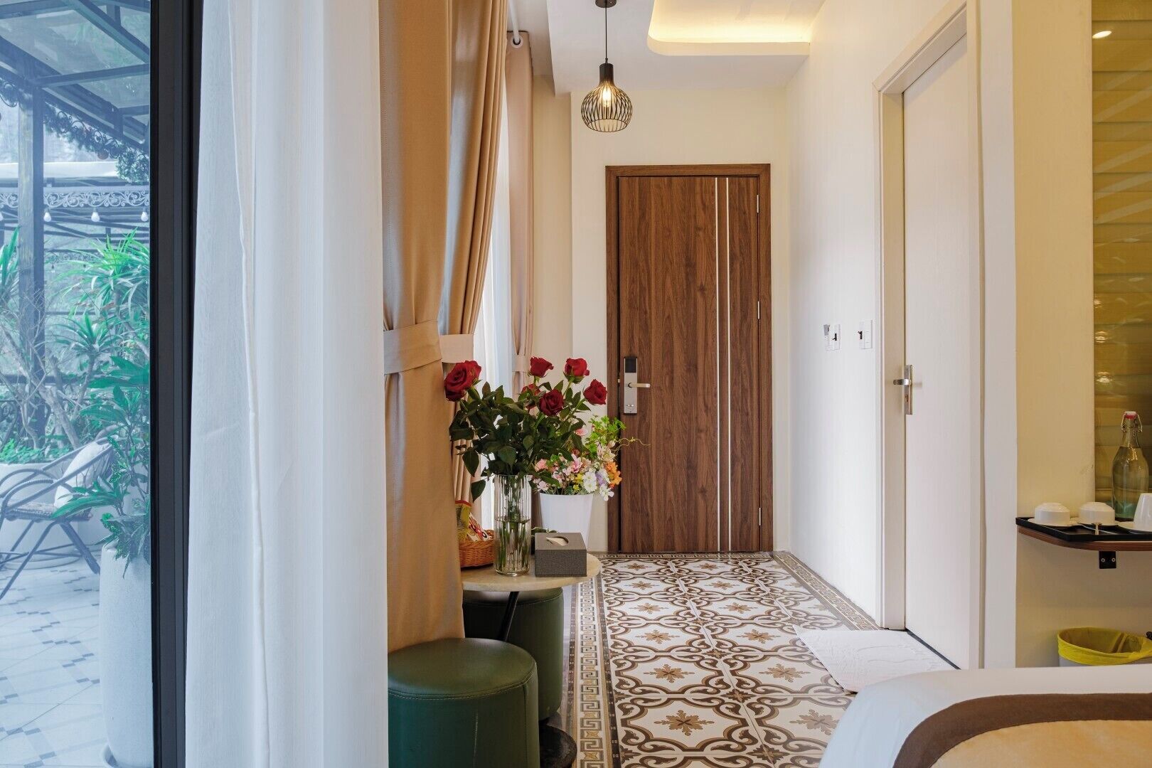 Un pasillo con puerta de madera, un florero, piso estampado y una lámpara colgante.