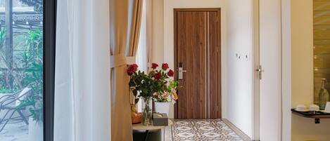 Un pasillo con puerta de madera, un florero, piso estampado y una lámpara colgante.
