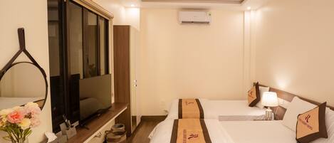 A hotel room with a TV, a bed with a brown headboard, a bedside table with a vase of flowers, and a wooden floor.