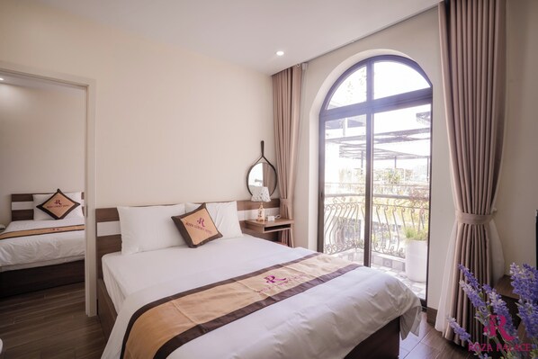Habitación de hotel con dos camas, un ventanal con cortinas, una mesita de noche con lámpara y vistas al exterior.