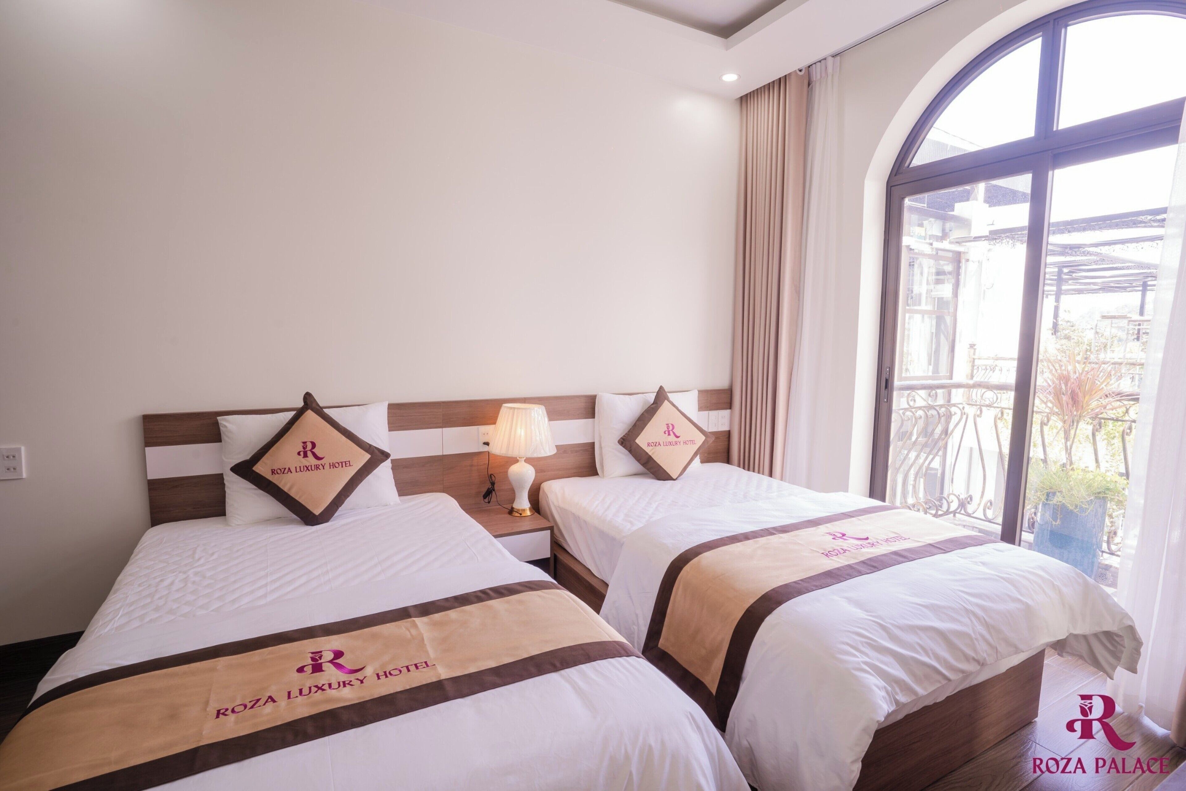 A hotel room with two beds, each with a headboard and a pillow featuring the hotel's logo.