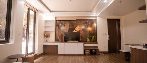 Una habitación de hotel moderna con una cama grande, un televisor, un mueble de madera, una mesita pequeña y un ventanal amplio.