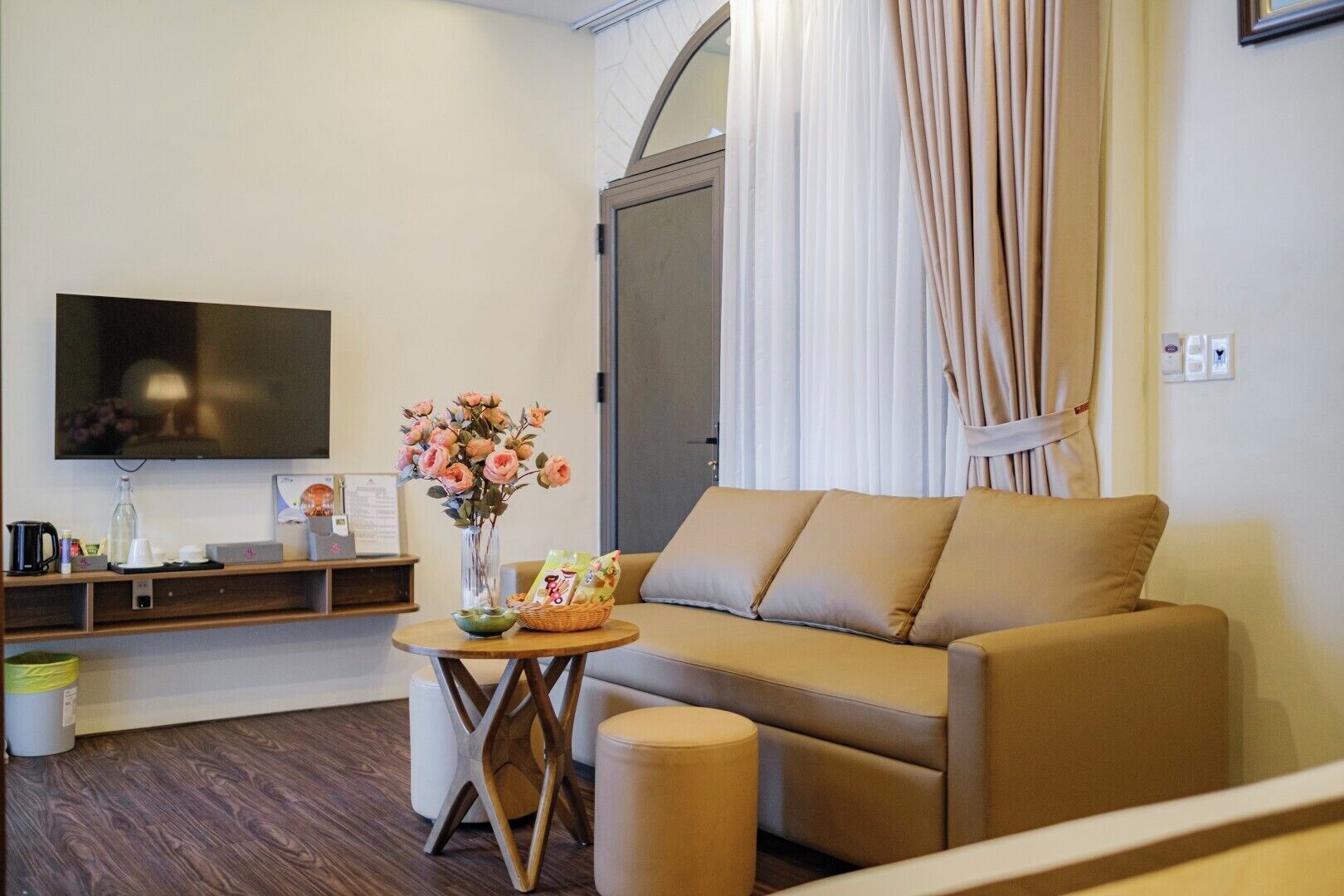 A modern living room with a sofa, a flat-screen TV, a vase with flowers, and a small table with a basket.