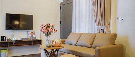 A modern living room with a sofa, a flat-screen TV, a vase with flowers, and a small table with a basket.