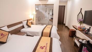 A hotel room with two beds, a desk, a TV, and a bathroom visible through a glass door.