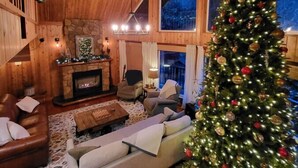 A cozy log cabin interior with a fireplace, a Christmas tree, and a large window.