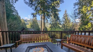 A deck with a fire pit, wooden benches, and a view of a forested mountain range.
