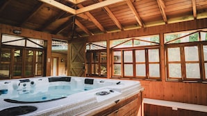 A wooden cabin with a hot tub, large windows, and a sloped ceiling.