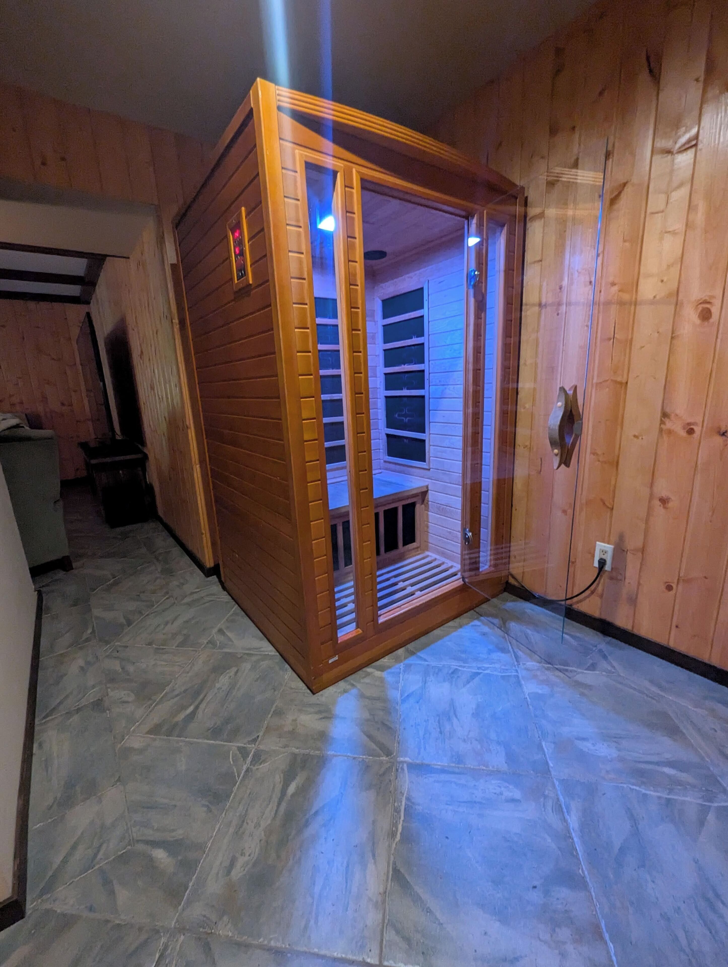 Un sauna en bois doté d’une porte en verre, d’un sol en pierre et d’un mur en bois.