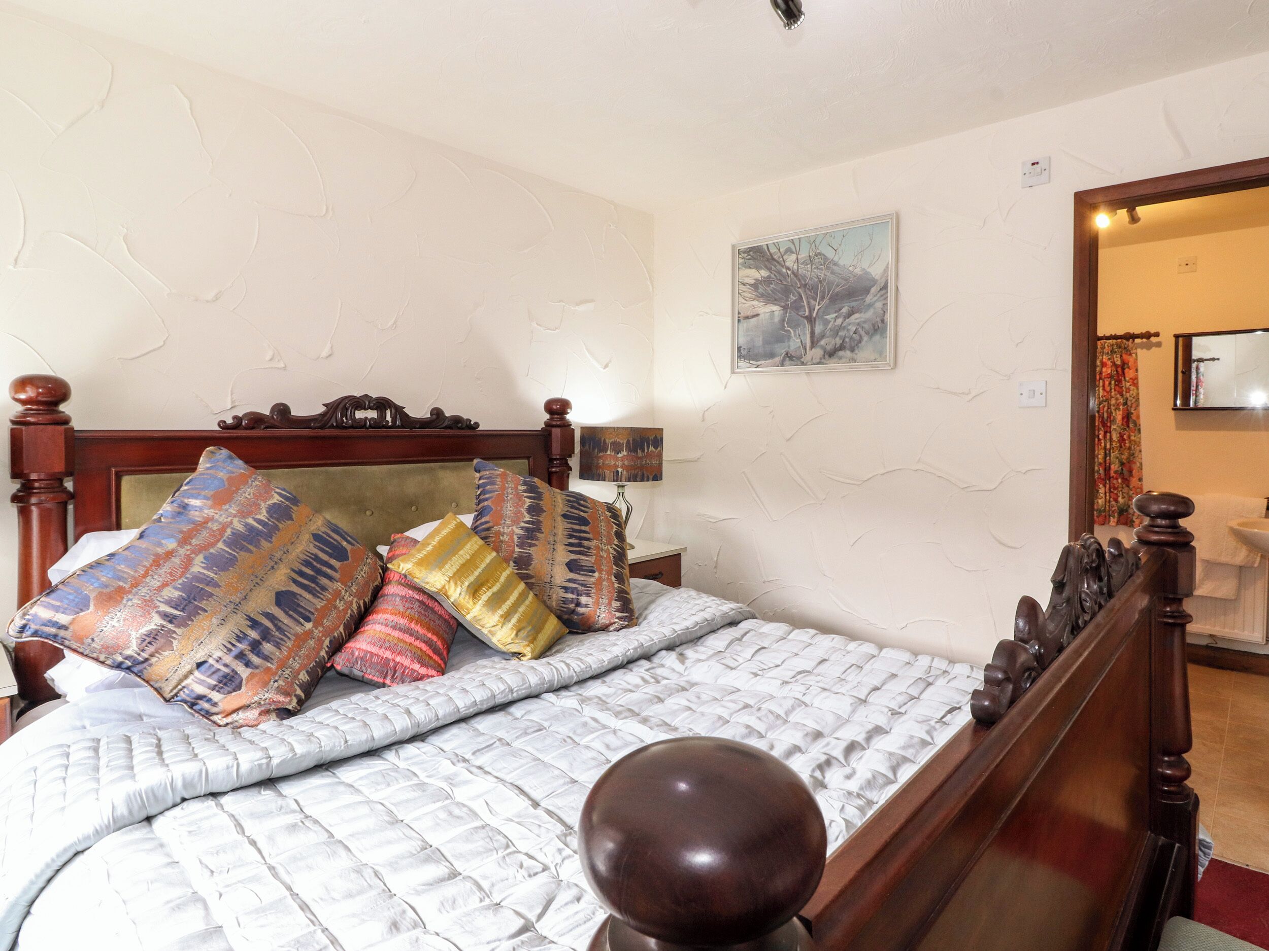A neatly made bed with patterned pillows, a wooden headboard, and a bedside table with a lamp.