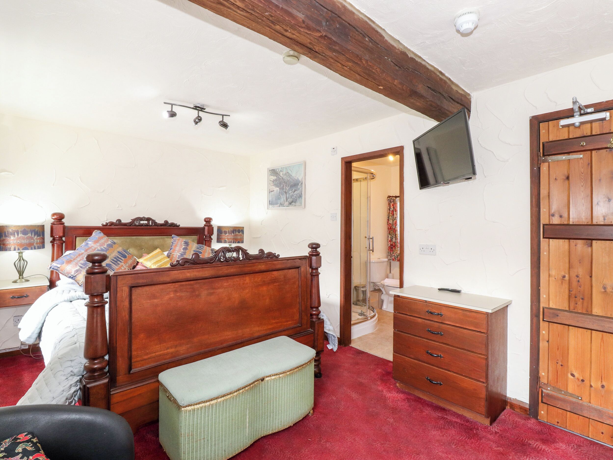 Un dormitorio con cama de madera, mesita de noche, televisor montado en la pared y armario de madera.