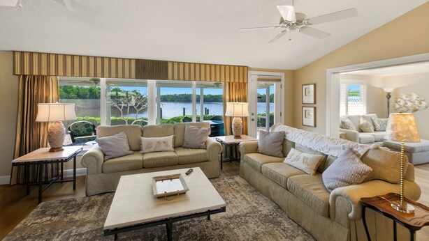 A spacious living room with a large window offering a view of a lake, two sofas, a coffee table, and a ceiling fan. - Spoonbill Lagoon with Fantastic Water Views of Palma Sola Bay! (Bradenton)