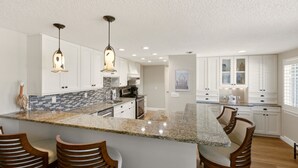 A modern kitchen with white cabinets, granite countertops, and pendant lighting. - Spoonbill Lagoon with Fantastic Water Views of Palma Sola Bay! (Bradenton)